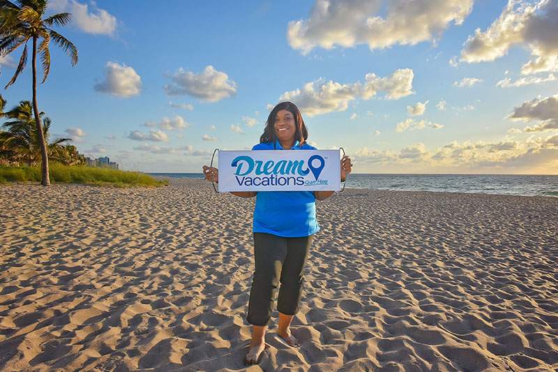 woman on the beach holding a Dream Vacations sign