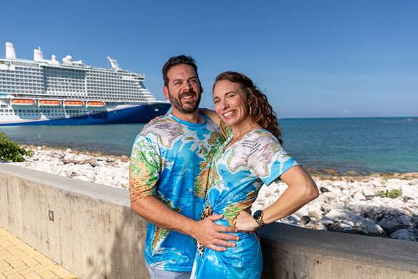 man and woman posing for a picture with a cruise ship behind them 