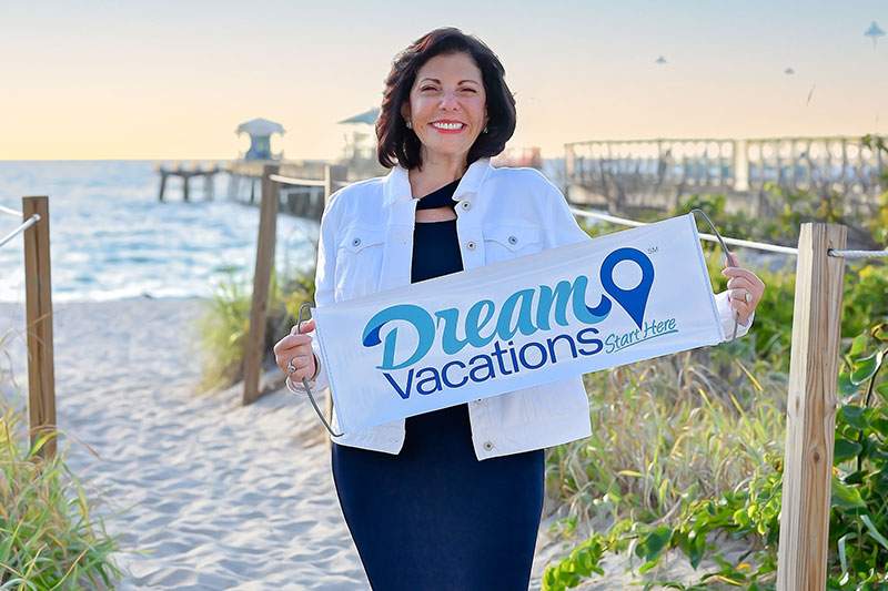 woman holing a Dream Vacations sign on the sand