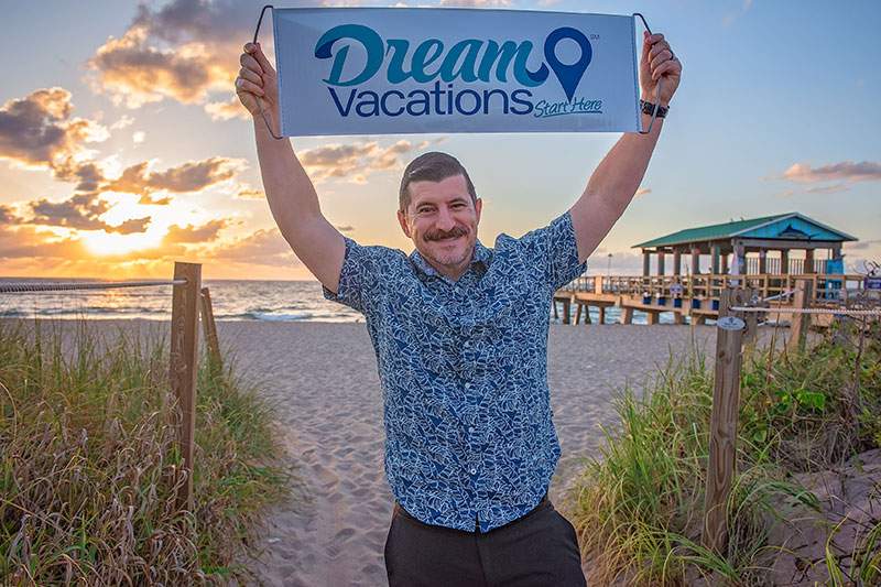 man on the sand holding Dream Vacations sign over his head