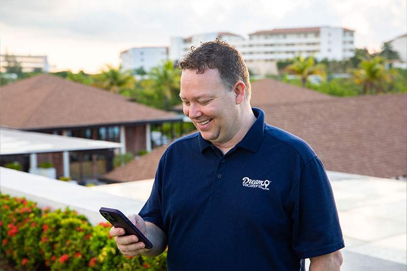 A Dream Vacations franchisee standing outdoors smiling at their phone