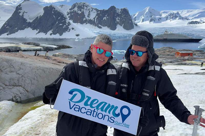 two men in snowsuits holding a Dream Vacations sign